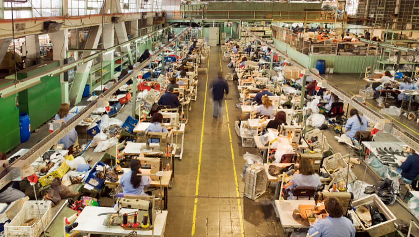 Busy factory floor with rows of workstations and workers producing goods.